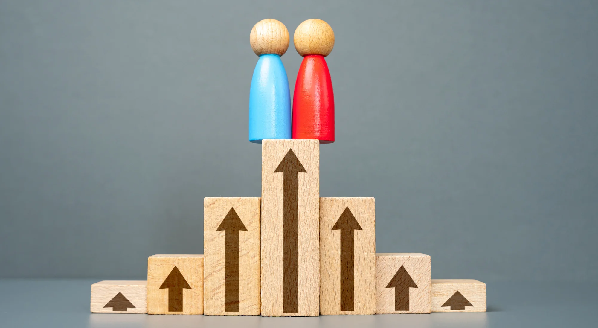 Wooden figures standing on ascending blocks representing rising housing maintenance standards, rental compliance and increasing expectations for property managers.